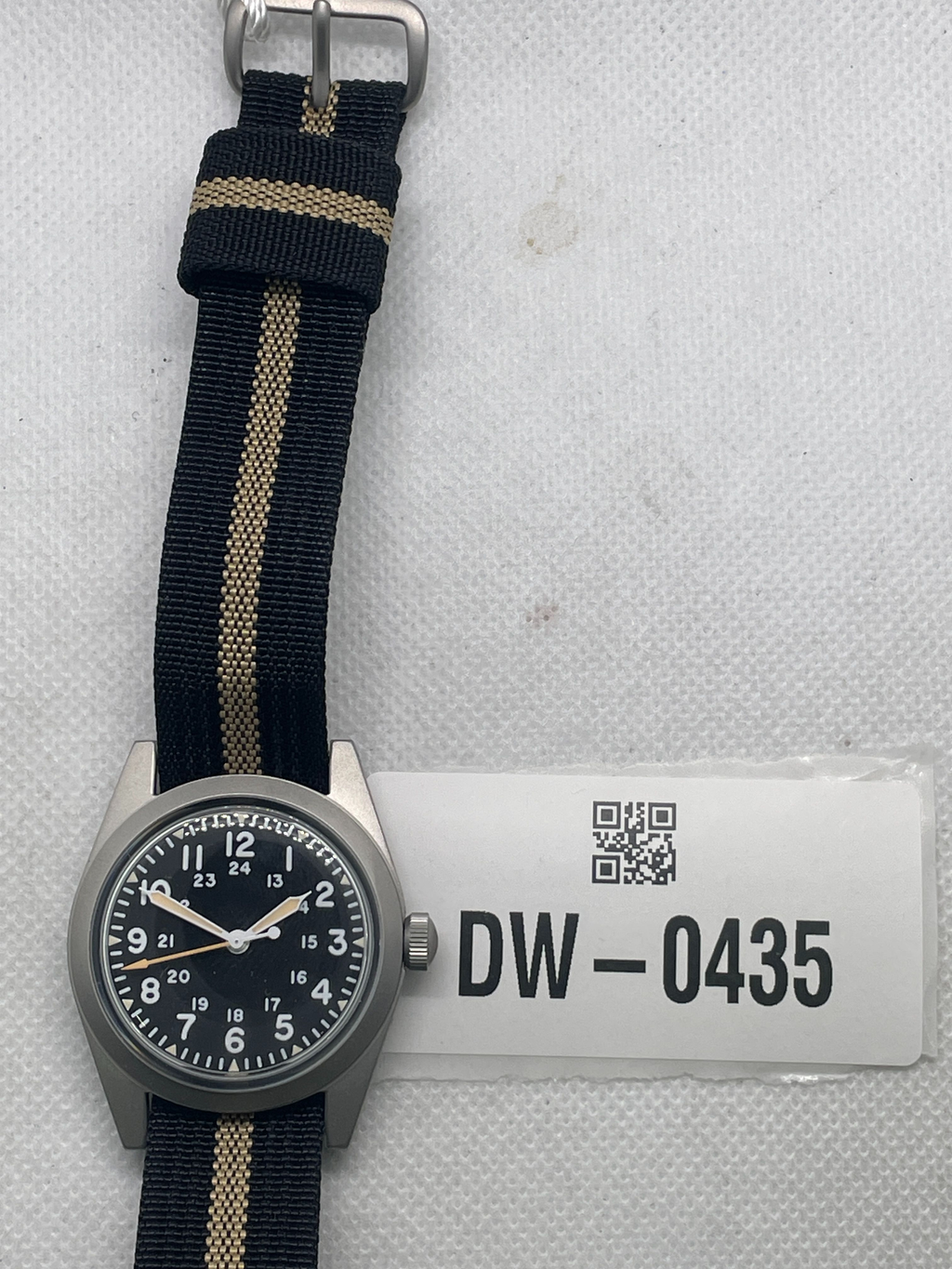 Pre-owned Rdunae field watch with a black 12- and 24-hour dial and black fabric strap with a tan stripe, beside tag DW-0435.