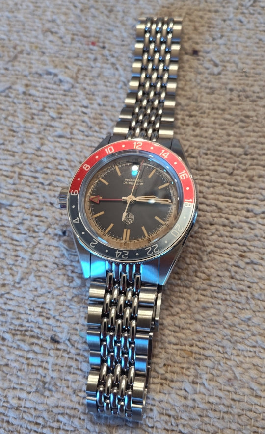 San Martin GMT watch lying on textured fabric with a red and blue 24-hour bezel and stainless steel bracelet.