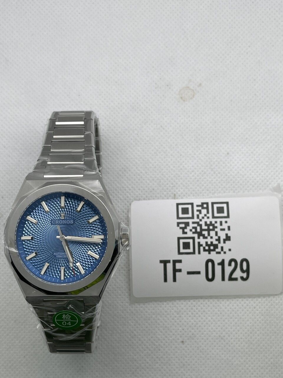 Cronos L6028 watch with blue textured dial and metal bracelet beside a TF-0129 inspection tag