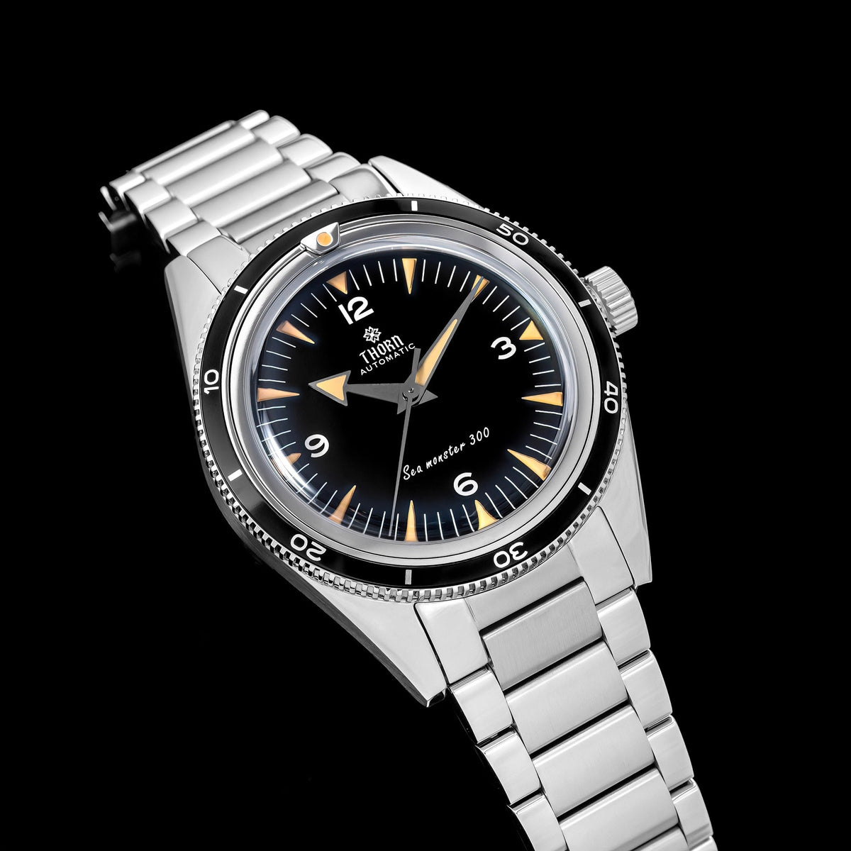 Angled close-up of a Thorn T026 watch with black dial and bezel and silver-tone bracelet on black